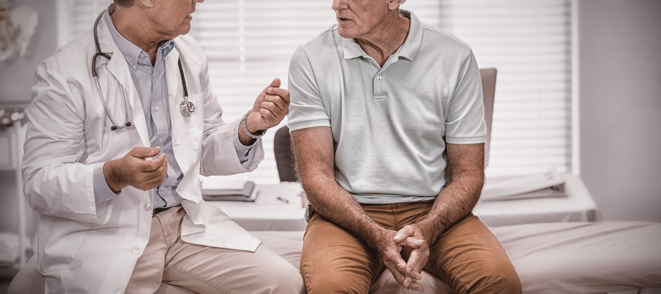 Médico conversa com paciente idoso sobre tratamento para câncer de próstata durante consulta urológica.