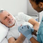 Médica urologista, mulher por volta dos 35 anos, explicando para seu paciente, homem por volta dos 65 anos, que está deitado em uma cama de hospital sobre o câncer de próstata e quais os sintomas mais comuns.