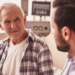 Médico urologista explicando para seu paciente mais velho sobre a importância da vigilância ativa no câncer de próstata em seu consultório médico.