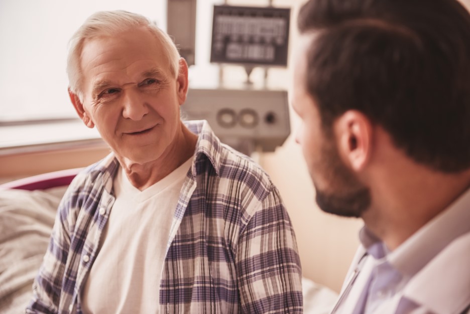 Médico urologista explicando para seu paciente mais velho sobre a importância da vigilância ativa no câncer de próstata em seu consultório médico. 