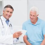 Médico urologista explicando para o seu paciente, homem por volta dos 60 anos, sobre o procedimento Rezum para hiperplasia prostática benigna.