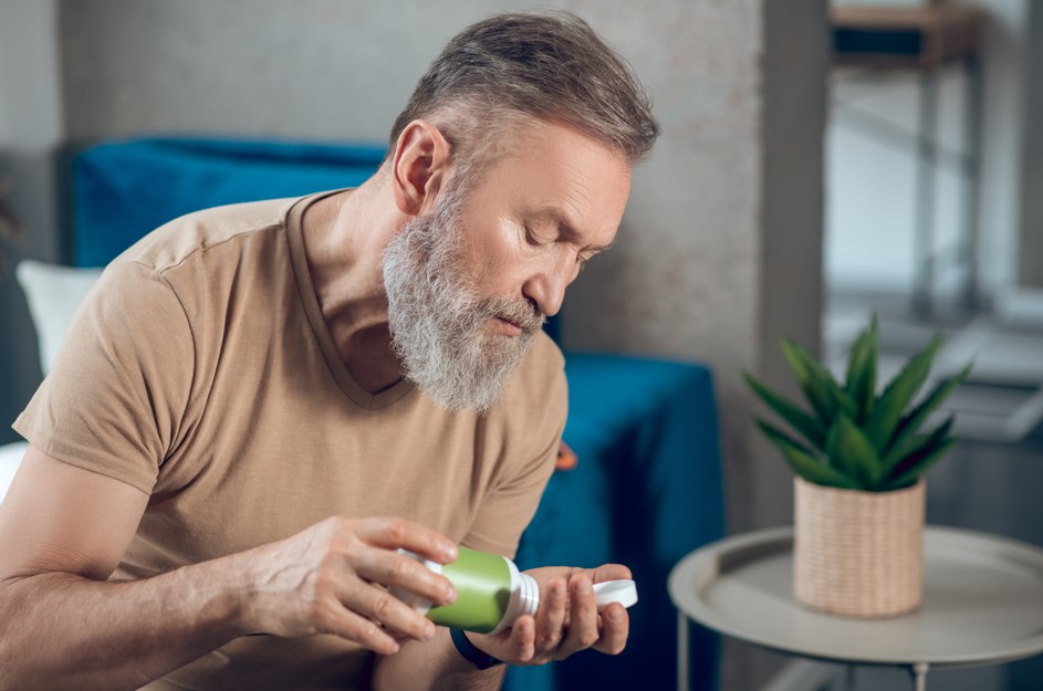 Homem, por volta dos 60 anos, com medicamentos em mãos pronto para tomar um remédio para próstata aumentada. 