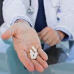 Médico urologista esticando mão com medicamentos que aumentam o PSA à sua frente.